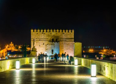 people are walking over the roman bridge in the spanish city cordoba towards the la mezquita cathedral.