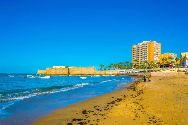 İspanyol Cadiz şehrinin arka planında bir otel ve savunma duvarı olan kumlu bir sahil manzarası.