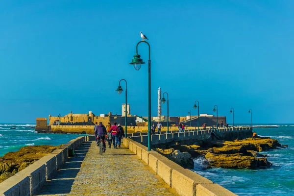 İnsanlar İspanya 'nın Cadiz kentindeki San Sebastian şatosuna giden dar bir tuğla yoldan geçiyorlar.