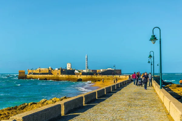 İnsanlar İspanya 'nın Cadiz kentindeki San Sebastian şatosuna giden dar bir tuğla yoldan geçiyorlar.