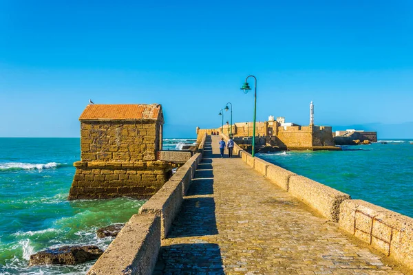 İnsanlar İspanya 'nın Cadiz kentindeki San Sebastian şatosuna giden dar bir tuğla yoldan geçiyorlar.