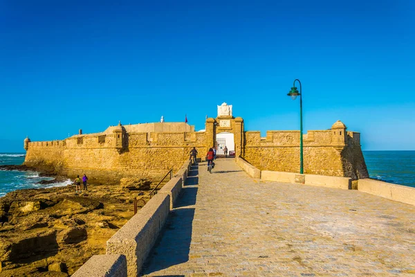 İnsanlar İspanya 'nın Cadiz kentindeki San Sebastian şatosuna giden dar bir tuğla yoldan geçiyorlar.