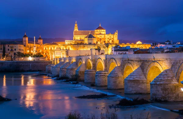 İspanyol şehri Cordoba 'daki La mezquita katedrali ile Guadalquivir nehri üzerindeki aydınlık Roma köprüsünün gece manzarası.