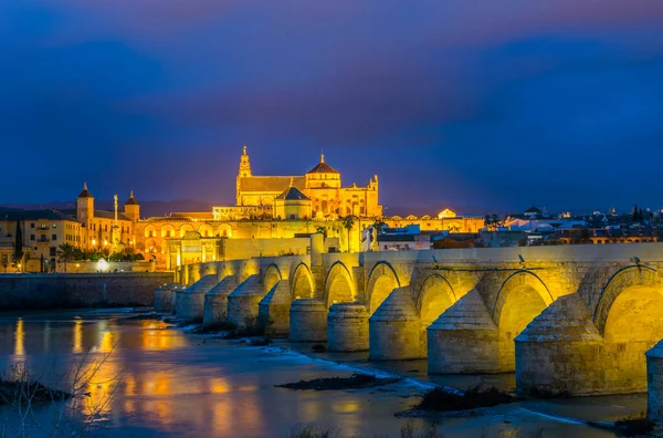 İspanyol şehri Cordoba 'daki La mezquita katedrali ile Guadalquivir nehri üzerindeki aydınlık Roma köprüsünün gece manzarası.