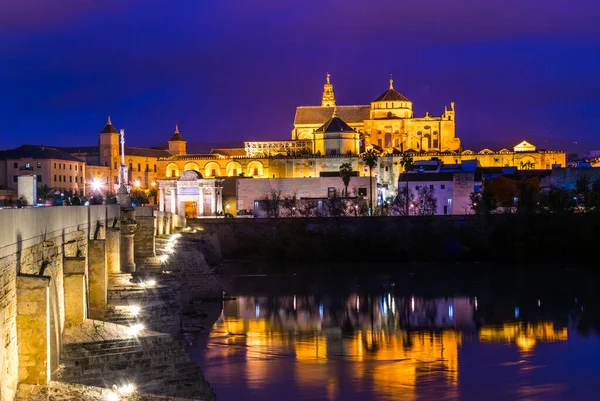 İspanyol şehri Cordoba 'daki La mezquita katedrali ile Guadalquivir nehri üzerindeki aydınlık Roma köprüsünün gece manzarası.