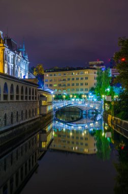 Ljubljanica nehrinin gece manzarası ve Sloven başkenti Ljubljana 'nın merkezindeki bitişik nehir kenarı.