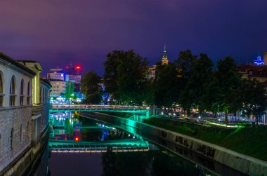 Ljubljanica nehrinin gece manzarası ve Sloven başkenti Ljubljana 'nın merkezindeki bitişik nehir kenarı.