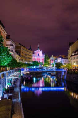 Üçlü köprüsü olan Ljubljanica nehrinin gece manzarası ve Sloven başkenti Ljubljana 'daki Fransisken kilisesi.