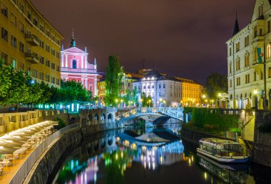 Üçlü köprüsü olan Ljubljanica nehrinin gece manzarası ve Sloven başkenti Ljubljana 'daki Fransisken kilisesi.