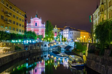 Üçlü köprüsü olan Ljubljanica nehrinin gece manzarası ve Sloven başkenti Ljubljana 'daki Fransisken kilisesi.