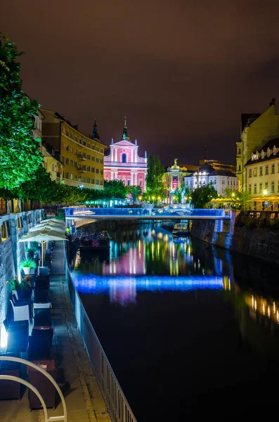Üçlü köprüsü olan Ljubljanica nehrinin gece manzarası ve Sloven başkenti Ljubljana 'daki Fransisken kilisesi.