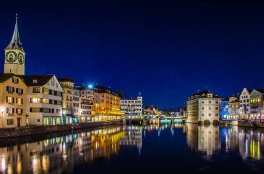 Munsterbrucke 'den Zürih' in gece manzarası. Sağda belediye binası ve solda Aziz Peter Kilisesi var.