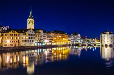Munsterbrucke 'den Zürih' in gece manzarası. Sağda belediye binası ve solda Aziz Peter Kilisesi var.