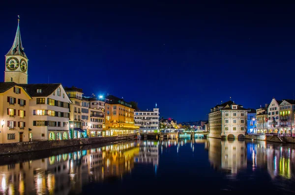 Munsterbrucke 'den Zürih' in gece manzarası. Sağda belediye binası ve solda Aziz Peter Kilisesi var.