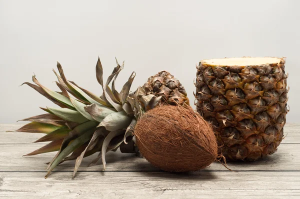 Kokos a napůl řez ananas na dřevěné desce — Stock fotografie