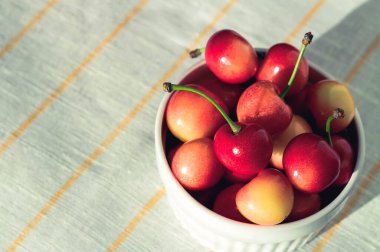 Taze kırmızı kiraz, beyaz kumaş arka planda bir kasede.