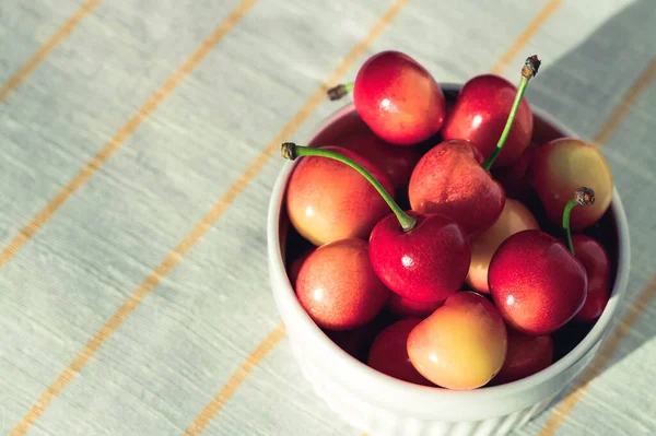 Taze kırmızı kiraz, beyaz kumaş arka planda bir kasede.