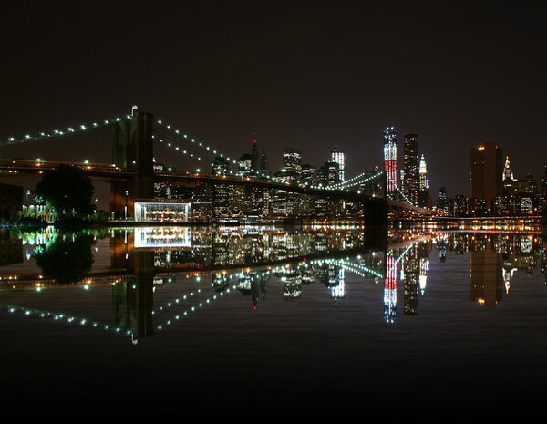 Brooklyn Bridge by night reflect in east river and new york skyline. freedom tower