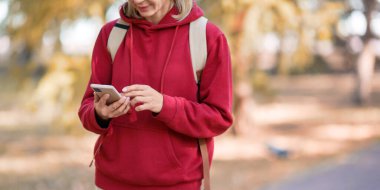 Dijital bağımlılık. Sonbaharda parkta yürüyen kişinin cep telefonuna sahip eller, yakın plan, seçilmiş odak.