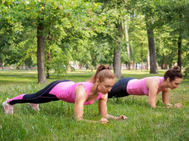 Takım açık hava takibi. Yazın halk parkında dirsek matkabında duran iki beyaz kadın seçici bir odak noktasındalar.