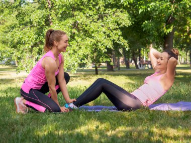 Antrenörle antrenman. Gülümseyen beyaz kadın yaz aylarında halka açık parkta koçun yardımıyla mekik çekiyor.