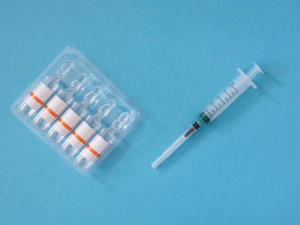 Disposable syringe and five glass ampoules in a blister on a blue background, close up, flatlay. — Zdjęcie stockowe