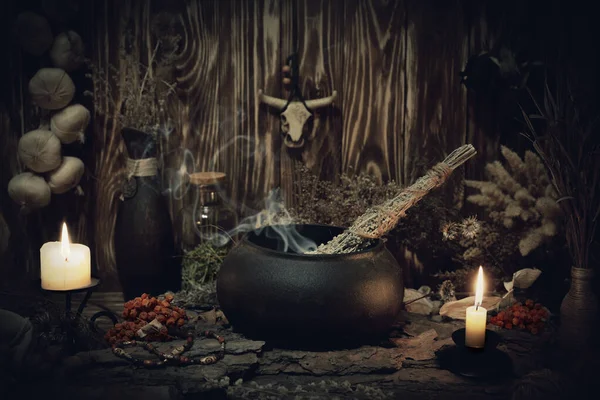 Altar de bruxa da floresta autêntica. Velas em chamas, ervas secas, caldeirão de ferro, abóbora fumadora, mojo de crânio de touros, molho de alho em fundo de madeira no escuro, chave baixa, foco seletivo. — Fotografia de Stock