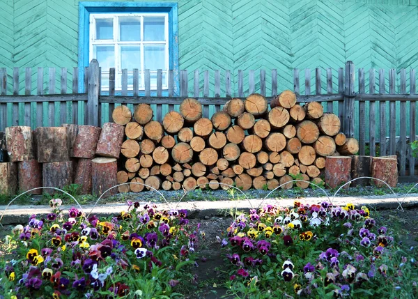 Woodpile near a wooden fence and pansies — Stock Photo, Image