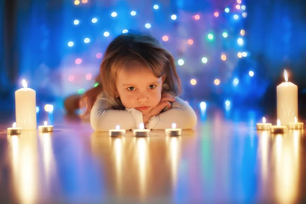 Menina pequena deitada no chão e olhando para velas — Fotografia de Stock
