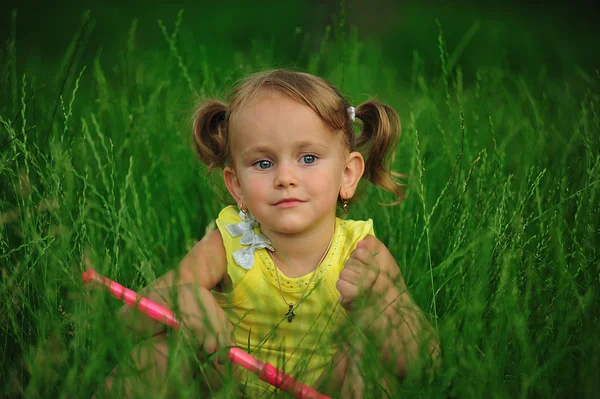 Улыбающаяся маленькая девочка сидит в траве — стоковое фото