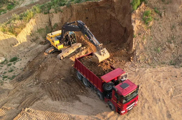 Excavator load the sand into dump truck. Aerial view of an backhoe on earthworks. Open pit development and sand mining. Loader digging ground for foundation pit. Earthmoving at construction site.