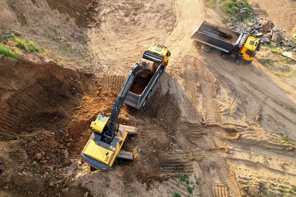 Excavator load the sand into dump truck. Aerial view of an backhoe on earthworks. Open pit development and sand mining. Loader digging ground for foundation pit. Earthmoving at construction site.