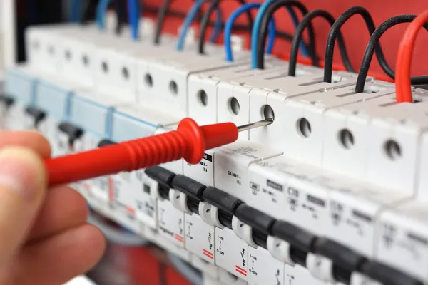 Hand of an electrician with multimeter probe at an electrical sw — Stock Photo, Image