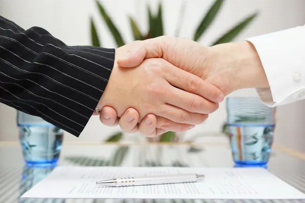 Empresário e empresária apertando as mãos sobre contrato assinado — Fotografia de Stock