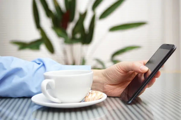 Бизнесмен пользуется современным мобильным телефоном и пьет кофе. Мбаппе — стоковое фото