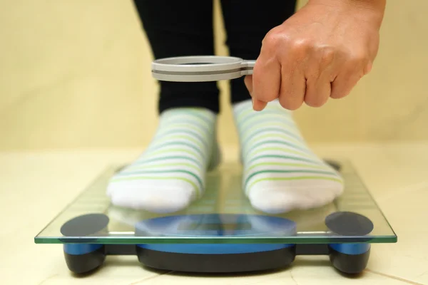 Woman feet on weighing scales looking weight over magnifying gla — Stock Photo, Image