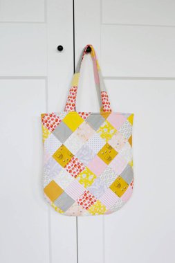 Beyaz gardırobun küçük siyah sapında asılı patchwork çanta