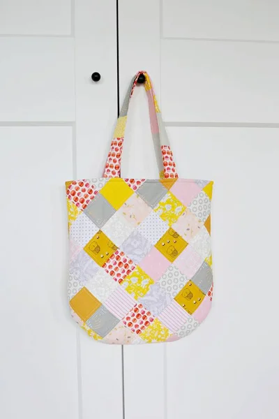 Patchwork tote bag hanging on the small black handle of the white wardrobe