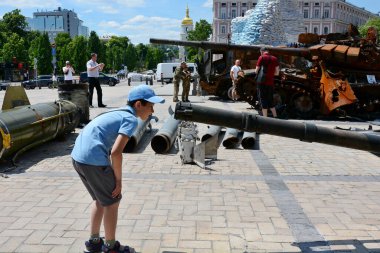 Çocuk, Kyiv 'in merkezinde sergilenen imha edilmiş Rus askeri zırhlı aracının silahını inceliyor.