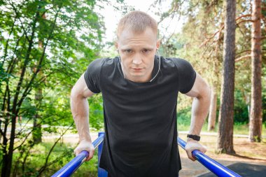 Parktaki paralel parmaklıklara triseps daldıran formda bir adam. Açık havada egzersiz yapıyor..