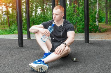 Omuzlarında havluyla sokakta oturmuş su içen genç bir adam..