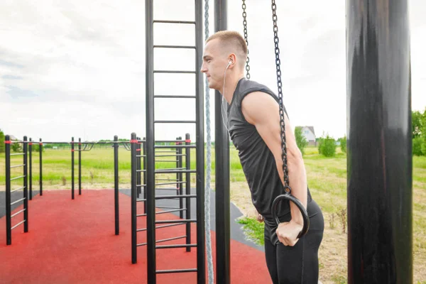 S'adapter jeune homme faisant de l'exercice avec des anneaux de gymnastique fitness rue. Homme musculaire faisant de l'exercice avec des anneaux. — Photo