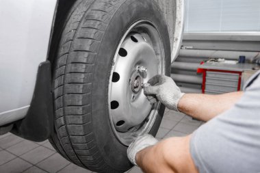 Tamirci yeni bir lastik takıyor. Tamirci modern bir arabanın direksiyonunu değiştiriyor tamirci de oto tamirhanesinde tekerlek değiştiriyor..