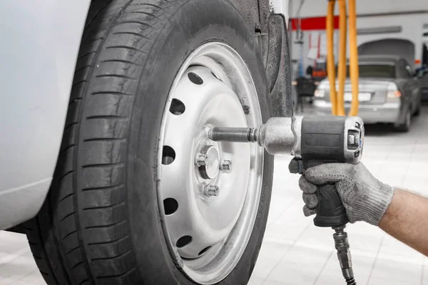 Tamirci yeni bir lastik takıyor. Tamirci modern bir arabanın direksiyonunu değiştiriyor tamirci de oto tamirhanesinde tekerlek değiştiriyor..