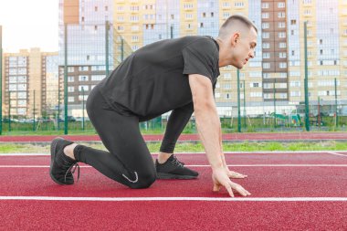 Stadyum pistinin başlangıç çizgisinde koşuya hazırlanan bir atlet. Genç kaslı sporcu stadyumdaki koşu bandının başında. Stadyumdaki pistin başında koşan ayağın.