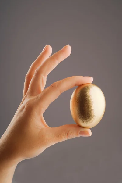 Mão segurando ovo dourado — Fotografia de Stock