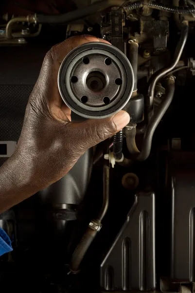 South African or American hand holding oil filter with modern car engine background — Stock Photo, Image