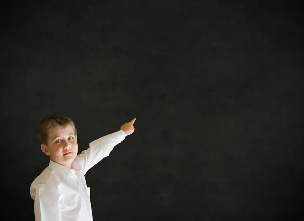 Boy dressed up as businessman pointing on blackboard background — Stock Photo, Image