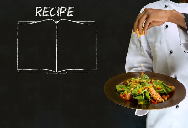 Chef with recipe book on chalk blackboard menu background — Stock Photo, Image