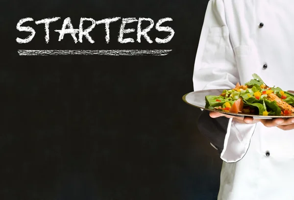 Chef-kok met krijt starters ondertekenen op blackboard achtergrond — Stockfoto